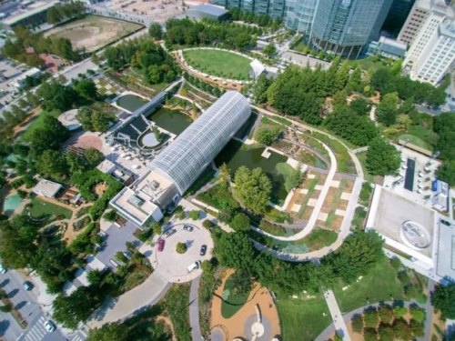 Aerial view of a green park with ponds, pathways, and modern buildings in the background.