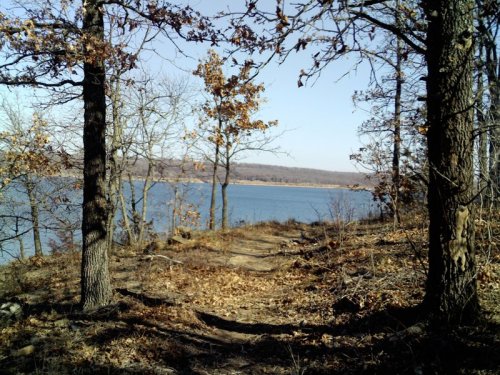 A serene lakeside view framed by trees, with autumn leaves and a clear blue sky in the background.