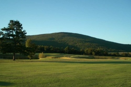 A serene landscape featuring a green golf course with a distant hill under a clear blue sky.