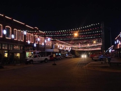 A festive street scene at night, adorned with colorful string lights and decorations illuminating the buildings.