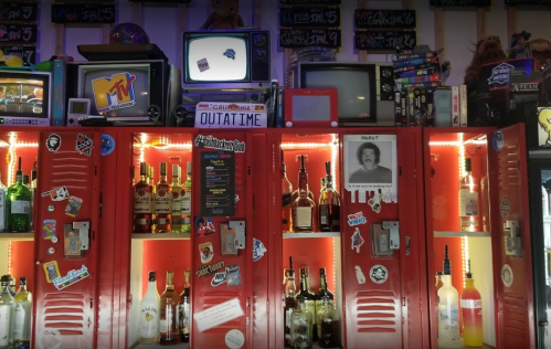 Colorful lockers filled with bottles, vintage TVs above, and retro decor, creating a nostalgic bar atmosphere.