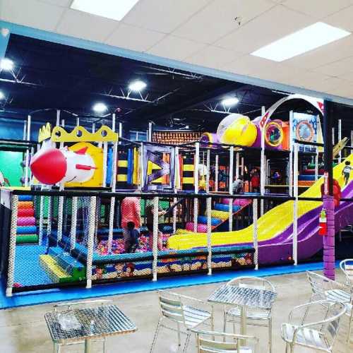 Colorful indoor playground with slides, climbing structures, and children playing in a ball pit.