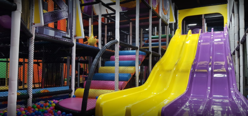 Colorful indoor playground featuring yellow and purple slides, climbing structures, and ball pits.