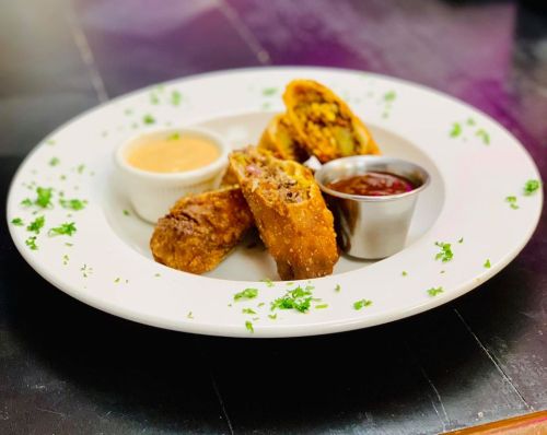 A plate with crispy fried rolls, served with dipping sauces and garnished with parsley.