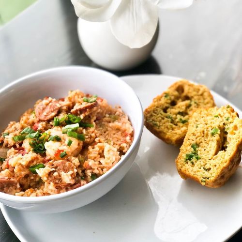 A bowl of rice with sausage and green onions, served with slices of cornbread on a white plate.