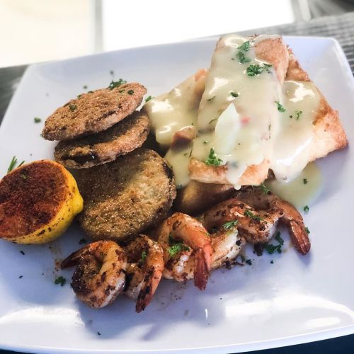 A plate of fried fish topped with sauce, shrimp, fried green tomatoes, and a grilled lemon slice, garnished with parsley.