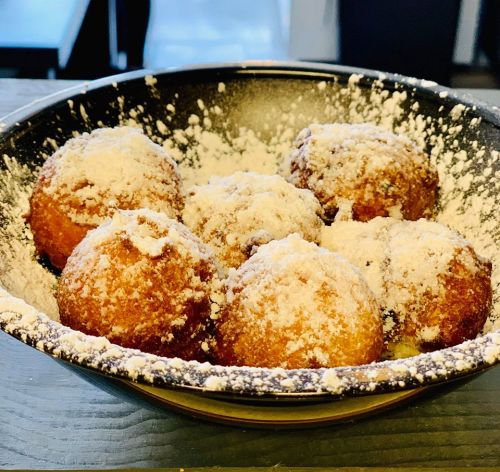 A bowl filled with six round, powdered sugar-coated fried dough balls.