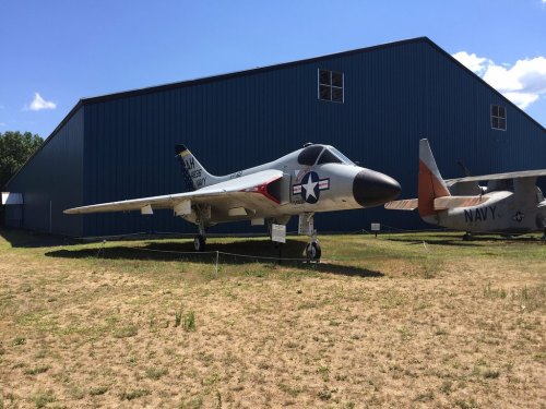 A military jet displayed outdoors next to a hangar, with a clear blue sky in the background.