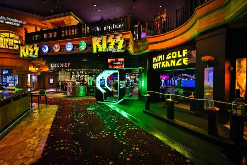 Vibrant interior of a themed entertainment venue featuring neon lights, a mini golf entrance, and a KISS-themed area.