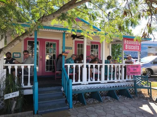 A colorful restaurant with outdoor seating, patrons enjoying meals on a sunny day, surrounded by trees.