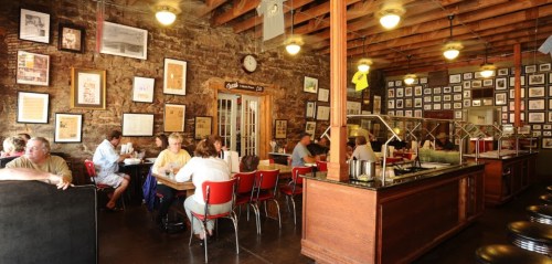 A bustling diner with wooden beams, brick walls, and framed photos, filled with patrons enjoying their meals.