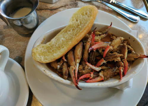 A dish of crab claws served with a slice of bread, accompanied by a small cup of sauce on the side.