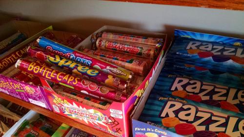 A colorful display of various candies, including Smarties, Spree, Bottle Caps, and Razzles in boxes on a shelf.