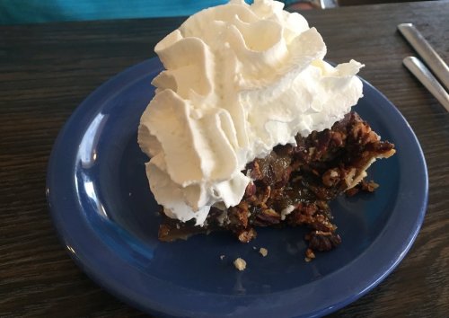 A slice of pecan pie topped with a generous dollop of whipped cream on a blue plate.