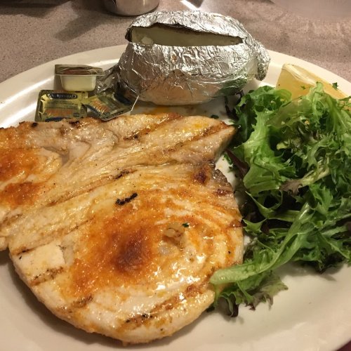 Grilled fish fillet with a baked potato wrapped in foil and a side of mixed greens on a plate.