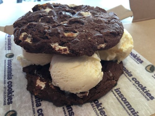 A towering dessert featuring two chocolate cookies with a generous scoop of vanilla ice cream in between.