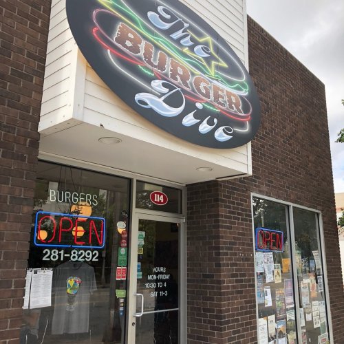 Exterior of The Burger Dive restaurant, featuring a neon "OPEN" sign and a menu displayed in the window.