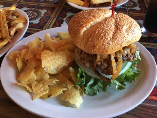 A sesame seed bun burger with lettuce, onions, and a side of potato chips on a plate.