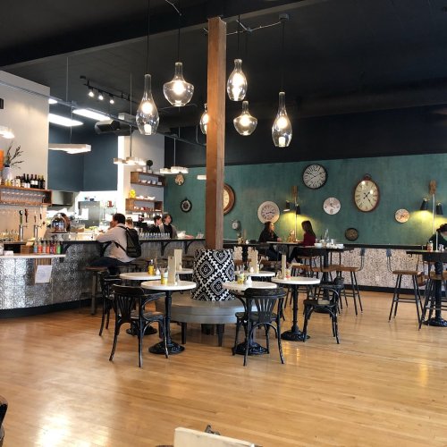 A cozy café interior with wooden floors, stylish lighting, and decorative clocks on the walls. Tables are set for dining.