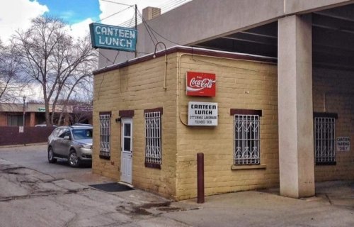 A small, yellow building with a sign reading "Canteen Lunch" and a Coca-Cola sign, located under a concrete structure.