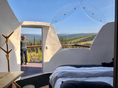 A modern room with a bed and large windows, showcasing a person enjoying a scenic view of nature outside.