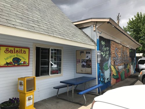Exterior of Salsita, a Mexican food restaurant, featuring colorful murals and a picnic table outside.