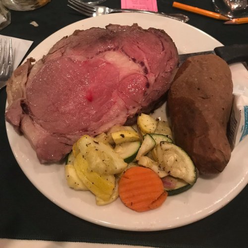 A plate featuring a large slice of prime rib, a baked potato, and a medley of grilled vegetables.