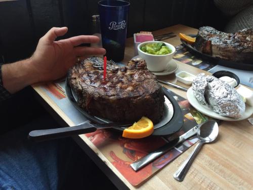A large steak on a sizzling plate with a candle, accompanied by a side of guacamole and a baked potato.