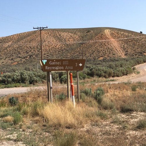 Sign for Garnet Hill Recreation Area with a dirt road and a hilly landscape in the background.
