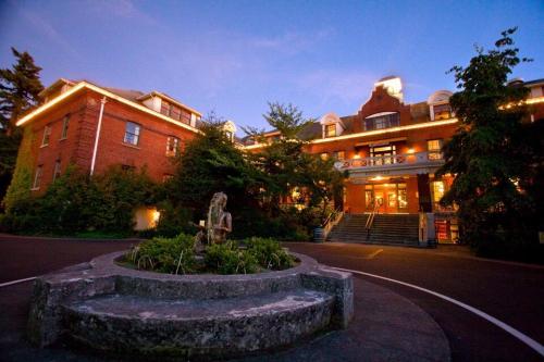 Historic brick building at dusk, featuring a landscaped fountain and illuminated entrance surrounded by trees.