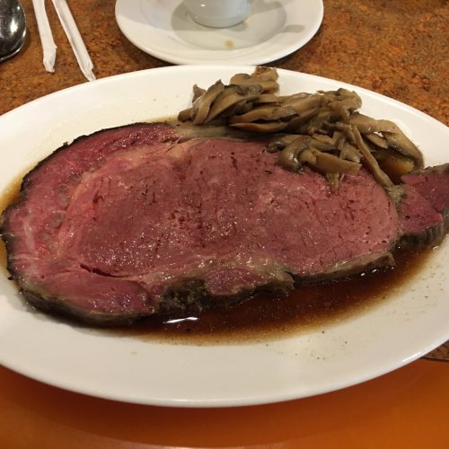 A plate of medium-rare prime rib served with sautéed mushrooms in a savory sauce.