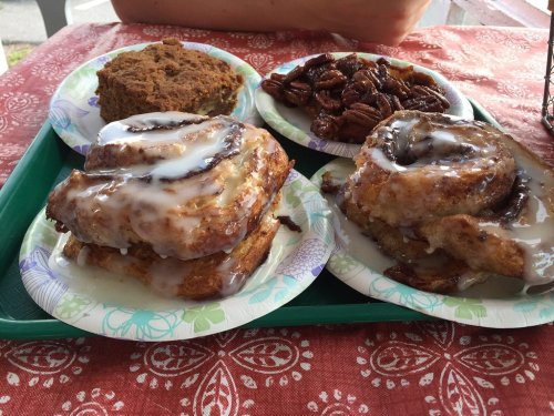 A tray with two cinnamon rolls drizzled with icing, a slice of cake, and a serving of pecans on paper plates.