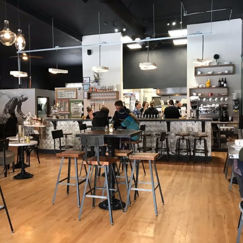 A modern café interior with a bar, seating area, and patrons enjoying their time. Bright lighting and stylish decor.