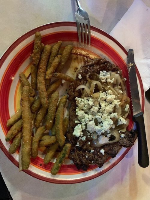 A plate with a grilled steak topped with onions and cheese, accompanied by crispy green beans and utensils.