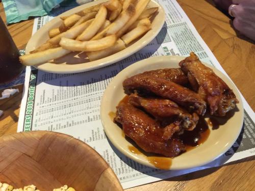 A plate of saucy chicken wings next to a side of golden French fries on a menu-covered table.