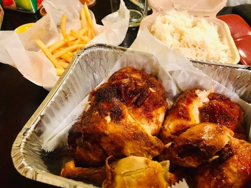 A takeout meal featuring roasted chicken, rice, and fries in containers on a table.
