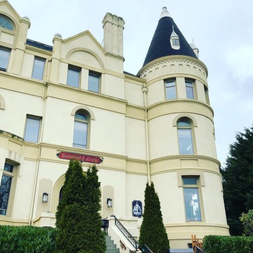 A historic building with a turret, featuring a restaurant sign and lush greenery in front.