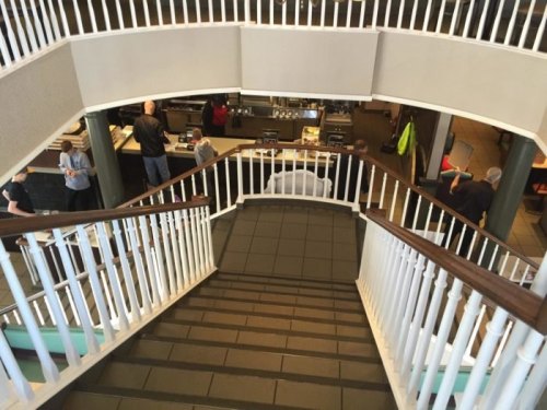 A view from above a staircase leading to a café, with people at the counter and seating areas visible.