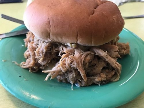 A pulled pork sandwich on a green plate, featuring tender, shredded meat piled high between a soft bun.