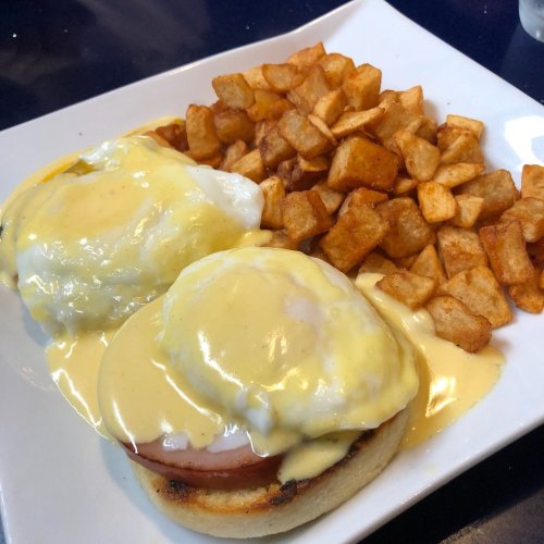 A plate of eggs Benedict with poached eggs, ham, and hollandaise sauce, served with crispy diced potatoes.