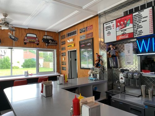 A retro diner interior with a counter, vintage car decor, and a menu board featuring classic food items and drinks.