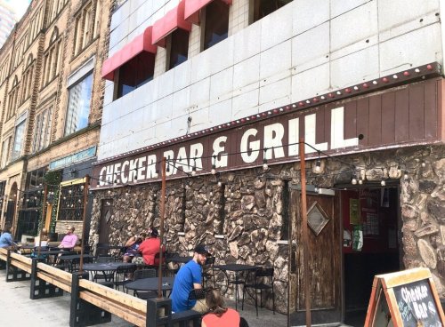 Exterior of Checker Bar & Grill with stone facade, outdoor seating, and a sign above the entrance.