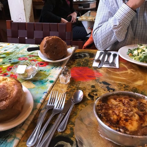 A table set with two large bread rolls, a salad, and a dish of crème brûlée, surrounded by utensils and a butter dish.