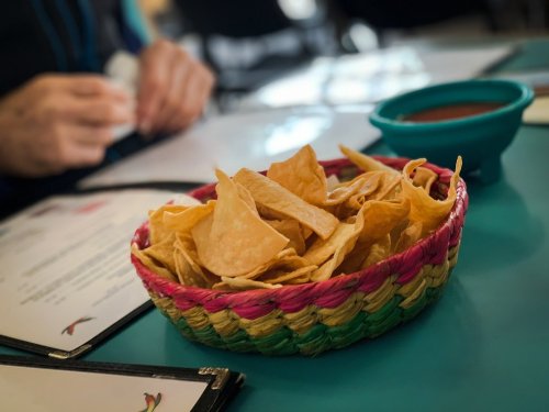A colorful basket filled with tortilla chips sits on a table, with a small bowl of salsa nearby.