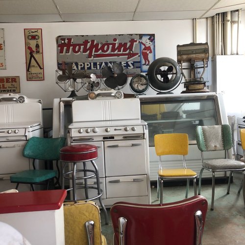 Vintage kitchen scene featuring old appliances, colorful chairs, and retro signage.