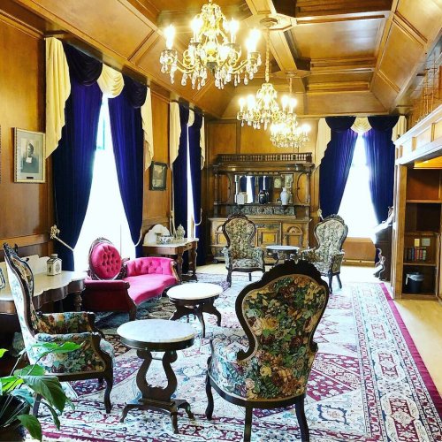Elegant room with wooden walls, chandeliers, plush seating, and rich curtains, featuring a vintage rug and decorative furniture.