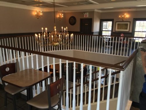 A view of a restaurant interior featuring a chandelier, wooden railings, and tables on a balcony overlooking the dining area.