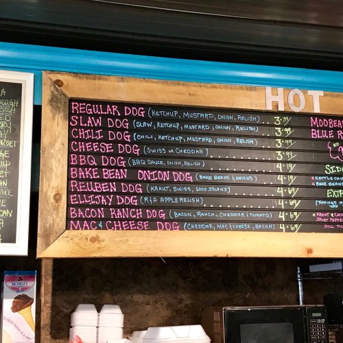 Menu board featuring various hot dog options with prices, including Slaw Dog, Chili Dog, and Mac & Cheese Dog.