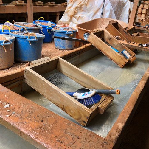 A workbench with wooden trays, cleaning tools, and buckets of sand in a workshop setting.