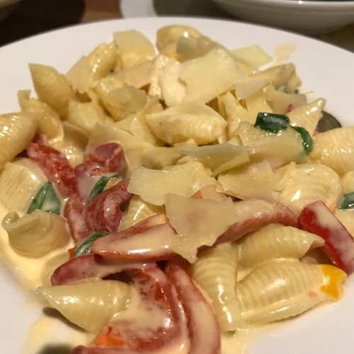 A plate of creamy pasta with shell noodles, red peppers, and cheese shavings.
